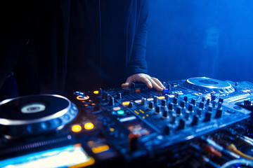 Hands of a DJ mixing music at a disco or concert with one hand on the switches and one held near the vinyl record on the turntable