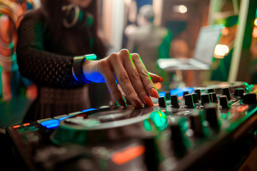 Blurred background with dj girl playing music and scratching tracks on professional dj midi controller.Modern disc jockey digital audio equipment for concerts or house party event.Stage lighting