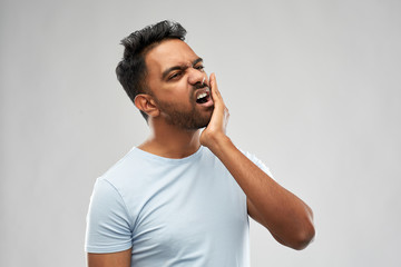 people, dentistry and health problem concept - indian man suffering from toothache over grey...