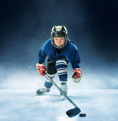 Little boy playing ice hockey at arena. A hockey player in uniform with equipment over a blue...