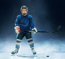 Little boy playing ice hockey at arena. A hockey player in uniform with equipment over a blue...