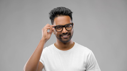 Obraz premium vision, education and people concept - happy smiling indian man in eyeglasses or student over grey background