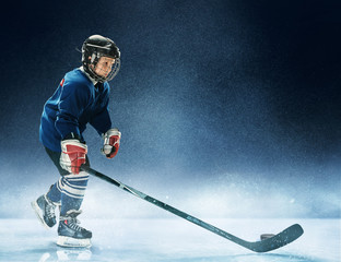 Little boy playing ice hockey at arena. A hockey player in uniform with equipment over a blue...