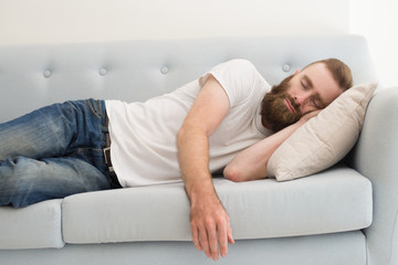 Bearded man lying and sleeping on sofa. Handsome guy dozing. Rest concept. Front view.