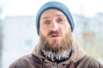 Young man with a beard covered with icicles and frozen droplets on the street after exercise. The...