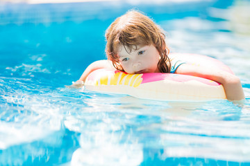 Child in swimming pool on inflatable donut float ring, learning how to swim, sad and tired