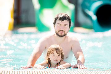 Happy family having fun together in outdoors swimming pool in water park (aquapark)