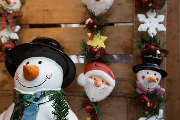 Snowman with black hat and carot as nose and green scarf next to a Santa Claus and other smaller snowman with pink scarf.