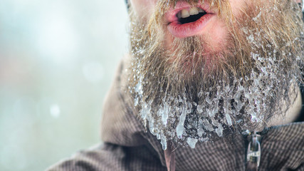 Beard in icicles. Part of the face of a smiling young man in a brown sports jacket. Concept of...