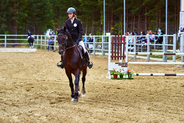 Young woman jockey in white black dress and black boots, takes part in equestrian competitions.