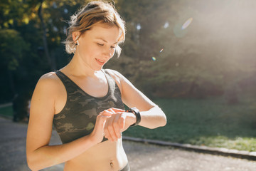 Fitness Woman In Wireless Earphones Using Smartwatch and runs in morning light