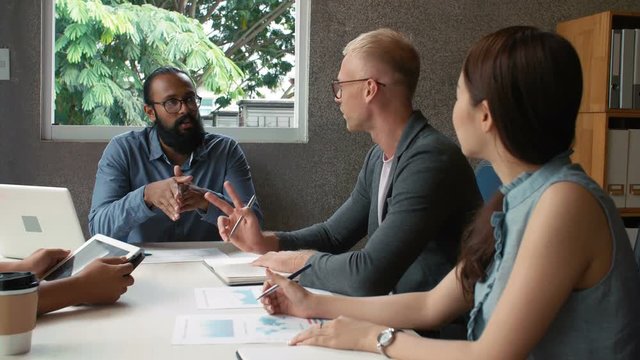 Multiethnic group of male and female office workers discussing financial situation and sharing creative ideas in conference room 