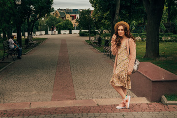 Smiling happy girl in dress and hat on a city street and looking at camera. in a hat, a dress in a flower and a jacket of warm colors