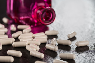 Close-up pile of white color medical pills on background vintage medical bottle made of red glass