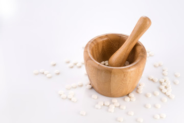 Close-up of small white tablets in a wooden mortar to be ground into powder. Preparation of medicinal mixtures.