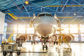 Aircraft in the aviation industrial hangar on maintenance, outside the gate bright light.