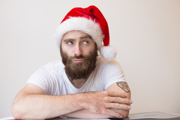 Thoughtful bearded man wearing Santa hat. Handsome guy looking away. Christmas preparation concept. Front view.