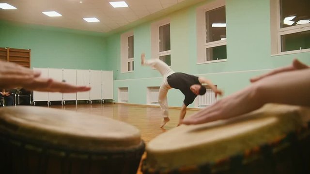 Fighter performs martial tricks with dance elements on background playing a two musical instruments atabaque