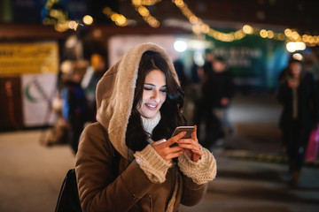 Close up of woman using smart phone on the street at night. In background street light.