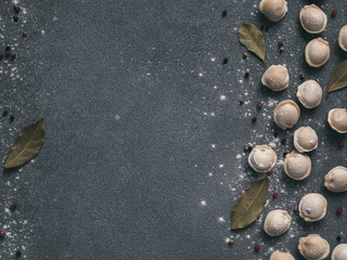 Pattern of frozen uncooked russian pelmeni with peppercorns and bay leaves on black background....