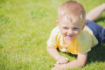 Cute toddler smiling boy lying at the green grass