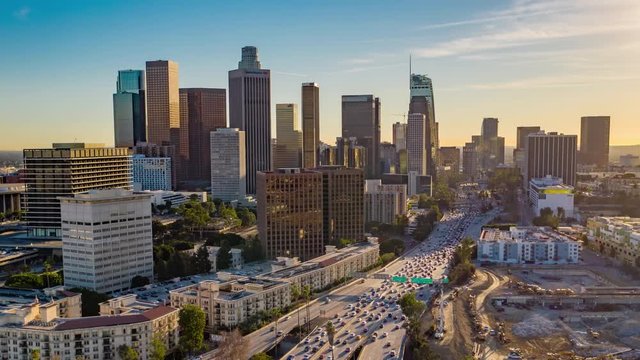 Cinematic urban aerial time lapse of downtown Los Angeles skyline with skyscrapers and freeway traffic below.