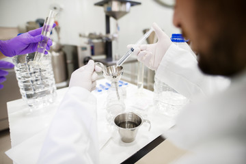 Fototapeta premium Close up of chemist and his assistant checking water quality at lab. In hands syringe and lab equipment. Gloves and protective suit on.