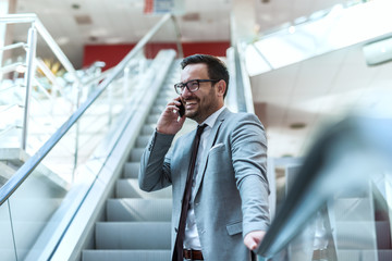 Close up of happy businessman standing on stairs and using smart phone. Suit and eyeglasses on.