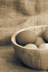 Eggs in a wooden bowl on a hessian background with toning