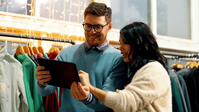 sale, shopping, fashion and technology concept - happy couple with tablet pc computer choosing clothes at vintage clothing store