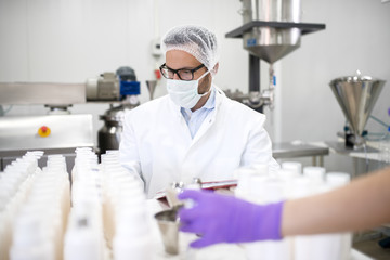 Chemist doing quality check for liquid soap. Protective suit and mask on.