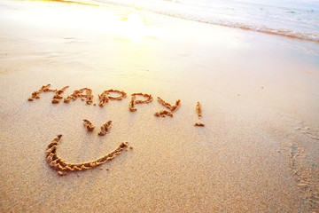 Happy letters handwritten in sand on beach