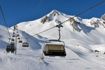 Ski resort with cable cars or aerial lift and ski-lift moving above the ground against winter landscape with mountains