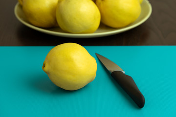 Ripe yellow quince and knife on blue cutting board.