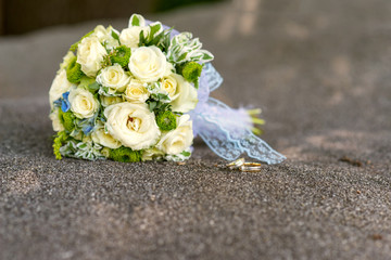 bridal bouquet of yellow roses and wedding rings over gray stone - close up