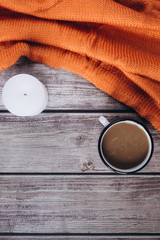 Winter cozy concept. Flat lay of orange knitted sweater, candle and coffee with milk  on wooden table