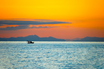 Silhouette of a ship on the background of mountains with orange glow of the sky in the evening sunset