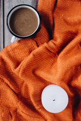 Winter cozy concept. Flat lay of orange knitted sweater, candle and coffee with milk  on wooden table
