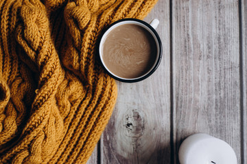Winter cozy concept. Flat lay of orange scarf, candle and coffee with milk drink on wooden table