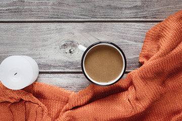 Winter cozy concept. Flat lay of orange knitted sweater, candle and coffee with milk  on wooden table