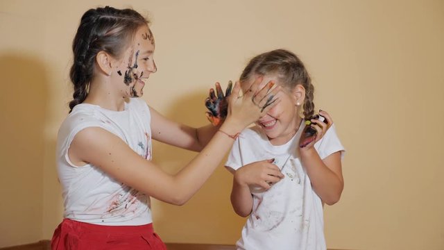 Happy adorable girls having fun and coloring each other with paints being messy in bright light, slow motion