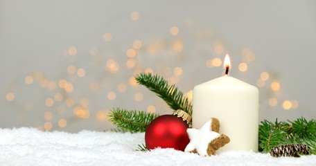 
Christmas background - candle with pine branches  in the snow with blurred lights in the background
