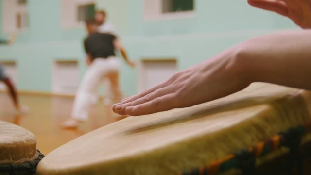 Playing a two musical instruments jembe or atabaque on background male fighter performs martial tricks in the sport gym