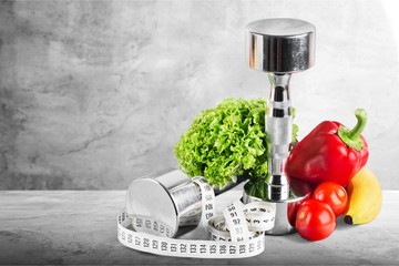 Dumbbells with bottled water , measuring tape and vegetables
