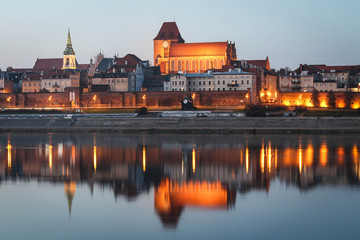 Fototapeta na wymiar TORUN, POLAND - Gothic Torun Cathedral and the panorama of the Old Town district in Torun with beautiful illuminations and evening sky water reflections