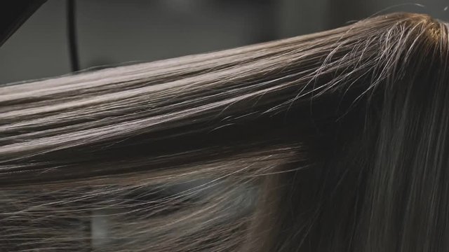 Close up Hairdresser drying and brushing hair of female in hair salon in slowmo.