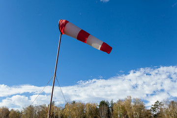red and white windsock wind sock on blue sky on the aerodrome, yellow field and clouds background