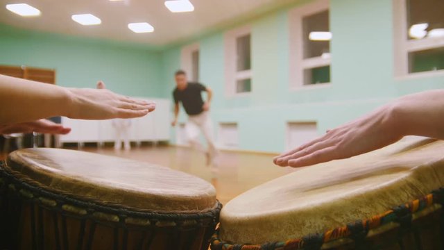 Fighter performs martial tricks with dance elements on background playing a two musical instruments jembe or atabaque