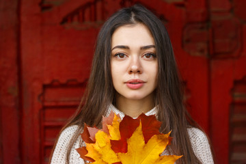 Portrait of a beautiful girl with a yellow leaf of maple in her hands. The girl is dressed in a warm, knitted sweater.