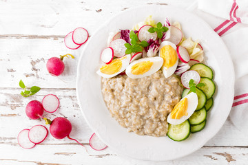 Oatmeal porridge with boiled egg and vegetable salad with fresh radish, cucumber and lettuce. Healthy dietary breakfast
